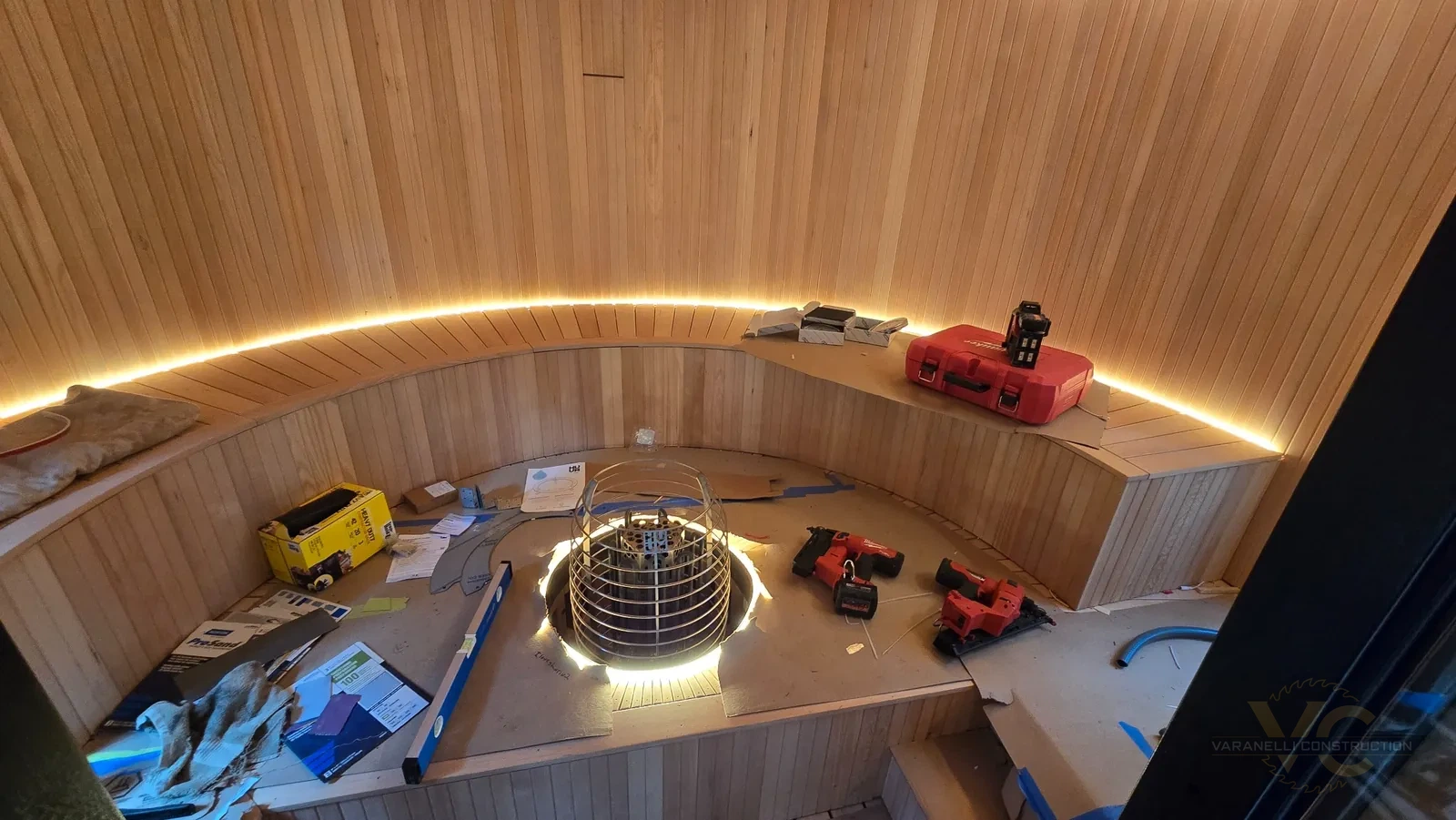 Round sauna interior nearing completion with curved wood bench, heater platform and perimeter lighting