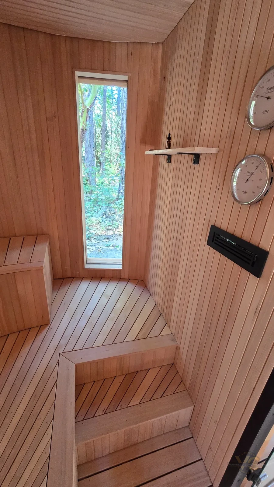 Finished custom sauna interior with tall forest window, stepped wood seating and wall controls
