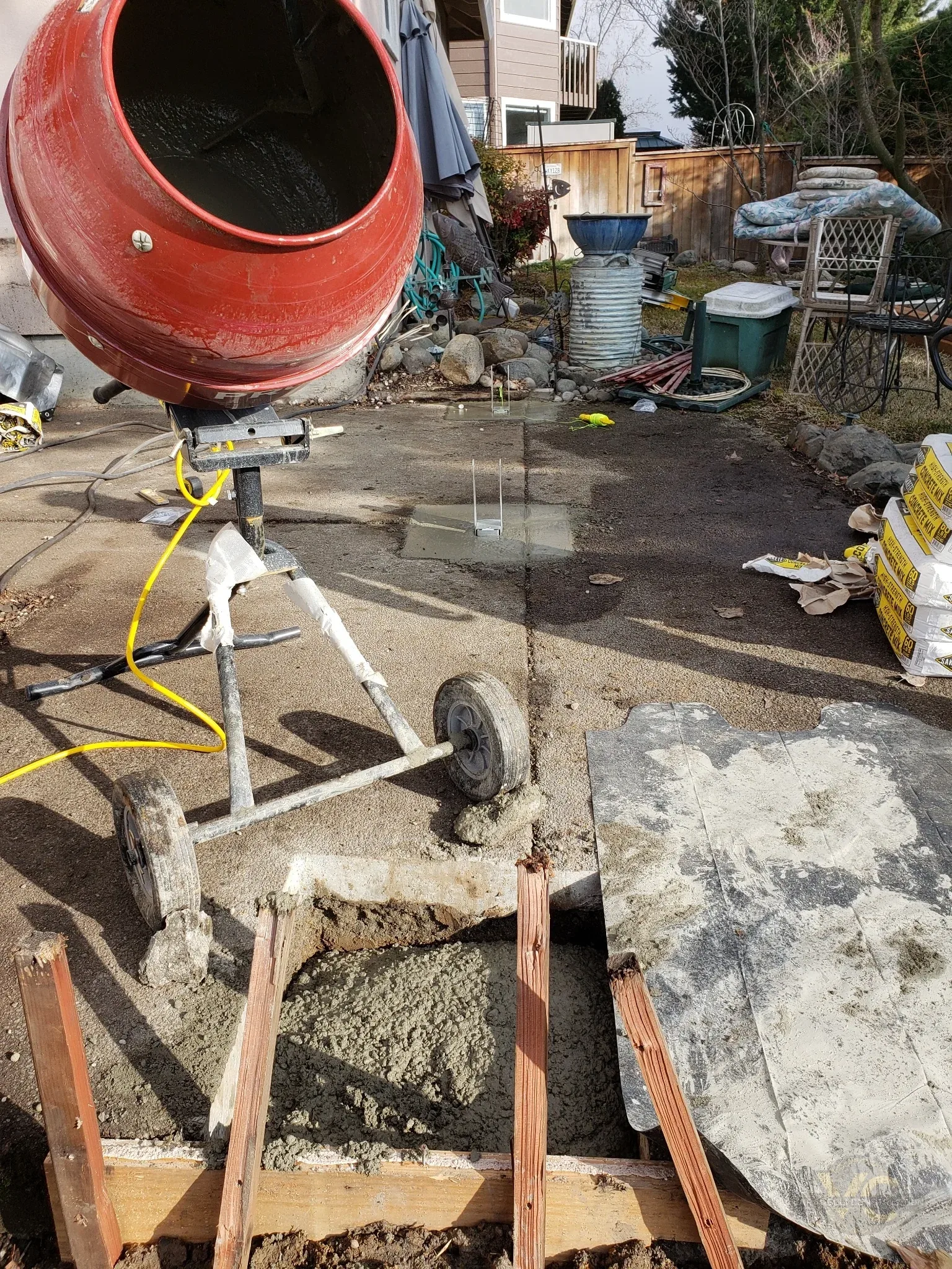 Fresh concrete footings being poured through cut sections of an existing patio slab for a Medford deck replacement