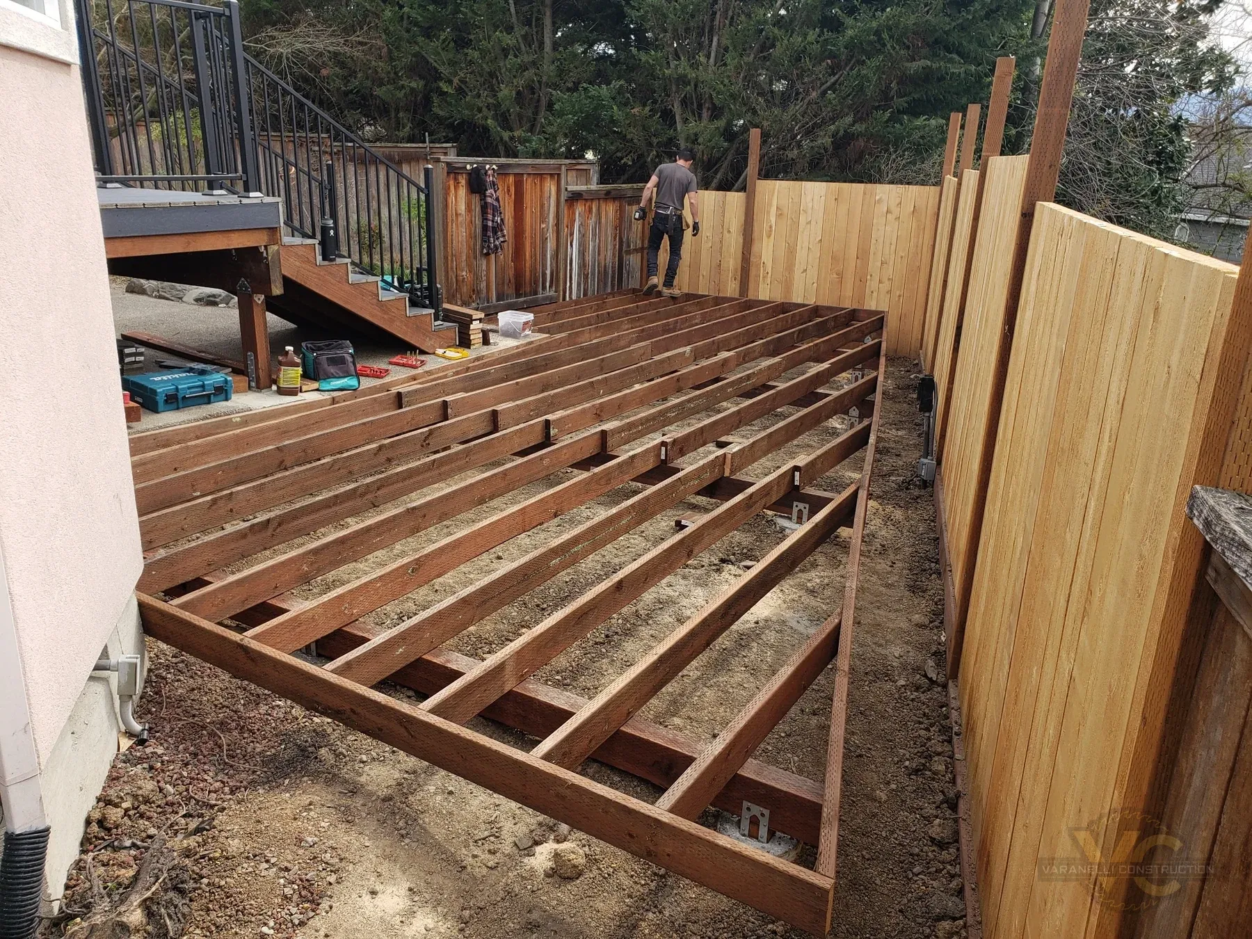 Pressure-treated framing for the lower level of a split-level Trex deck in Medford with the newly installed cedar fence beside it