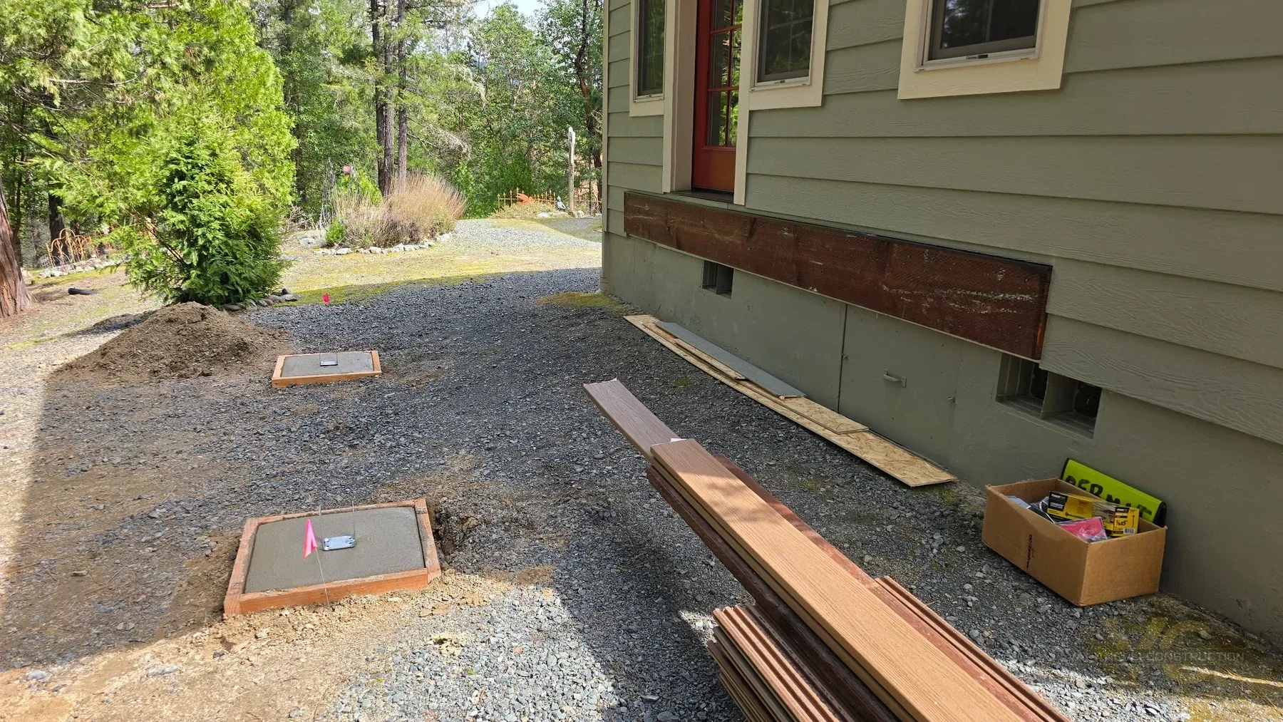 Concrete deck footings poured and Trex decking materials staged beside a Rogue River home